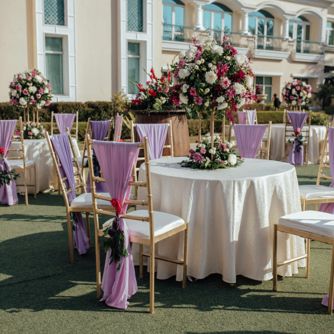 Outdoor event setup with floral centerpieces and lilac chair wraps